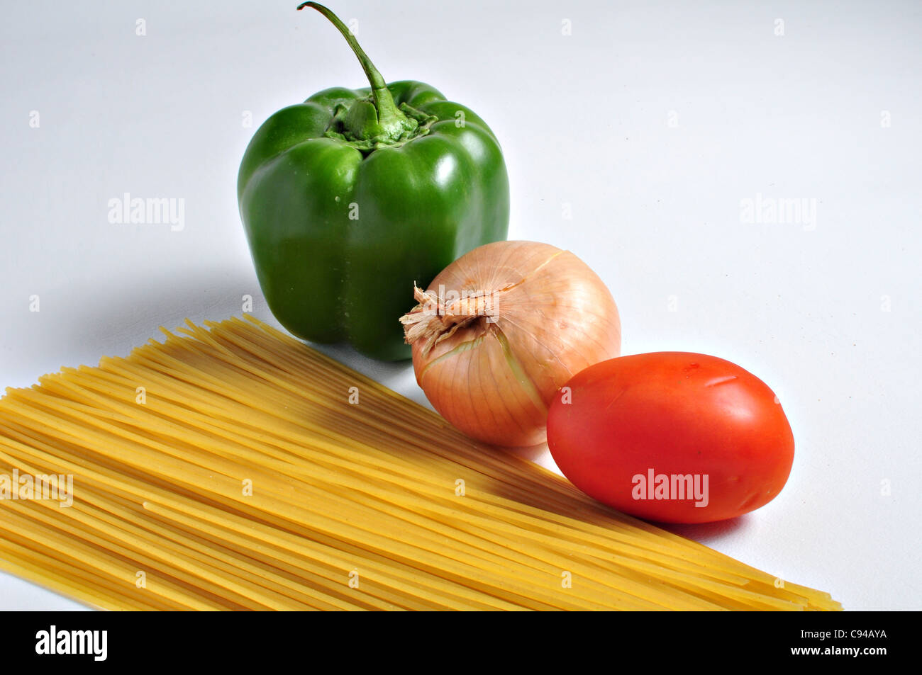 Gli spaghetti, pepe. cipolla e pomodoro sono in attesa su uno sfondo semplice per essere combinati in un pasto abbondante. Foto Stock