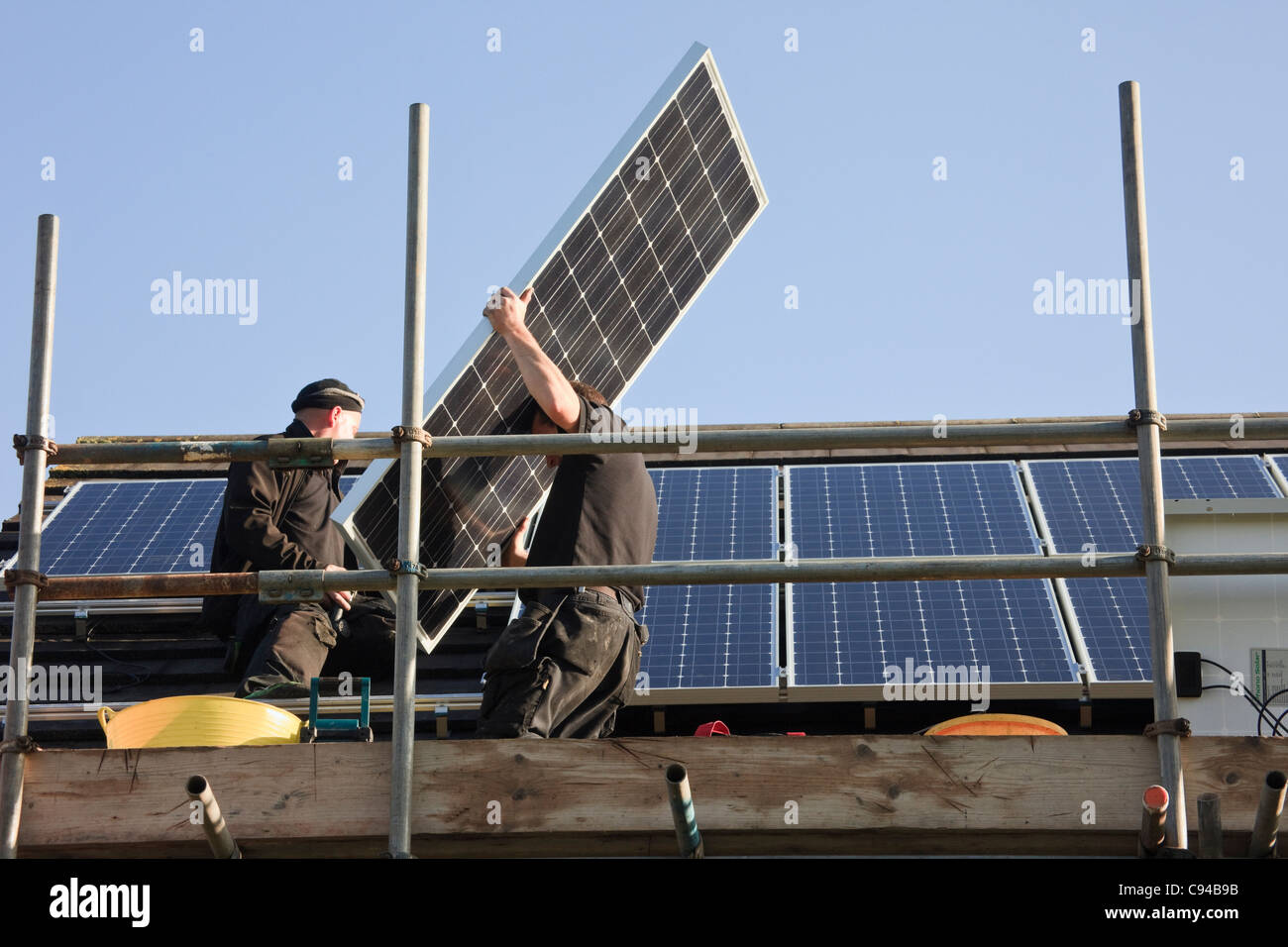 Operai il montaggio di nuovi pannelli solari per una casa residenziale tetto per i feed-in regime tariffario. Il Galles, Regno Unito, Gran Bretagna Foto Stock