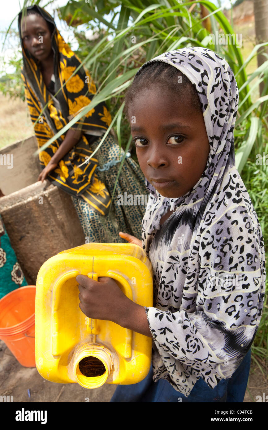 Una giovane ragazza attende per attingere acqua da un pozzo a Dar es Salaam, Tanzania Africa Orientale. Foto Stock