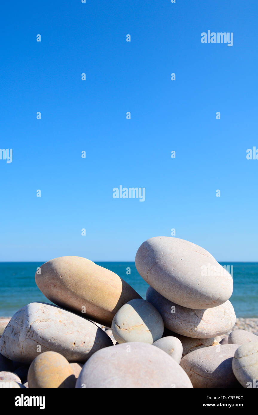 Ciottoli impilati su una spiaggia sotto un cielo blu chiaro. Foto Stock