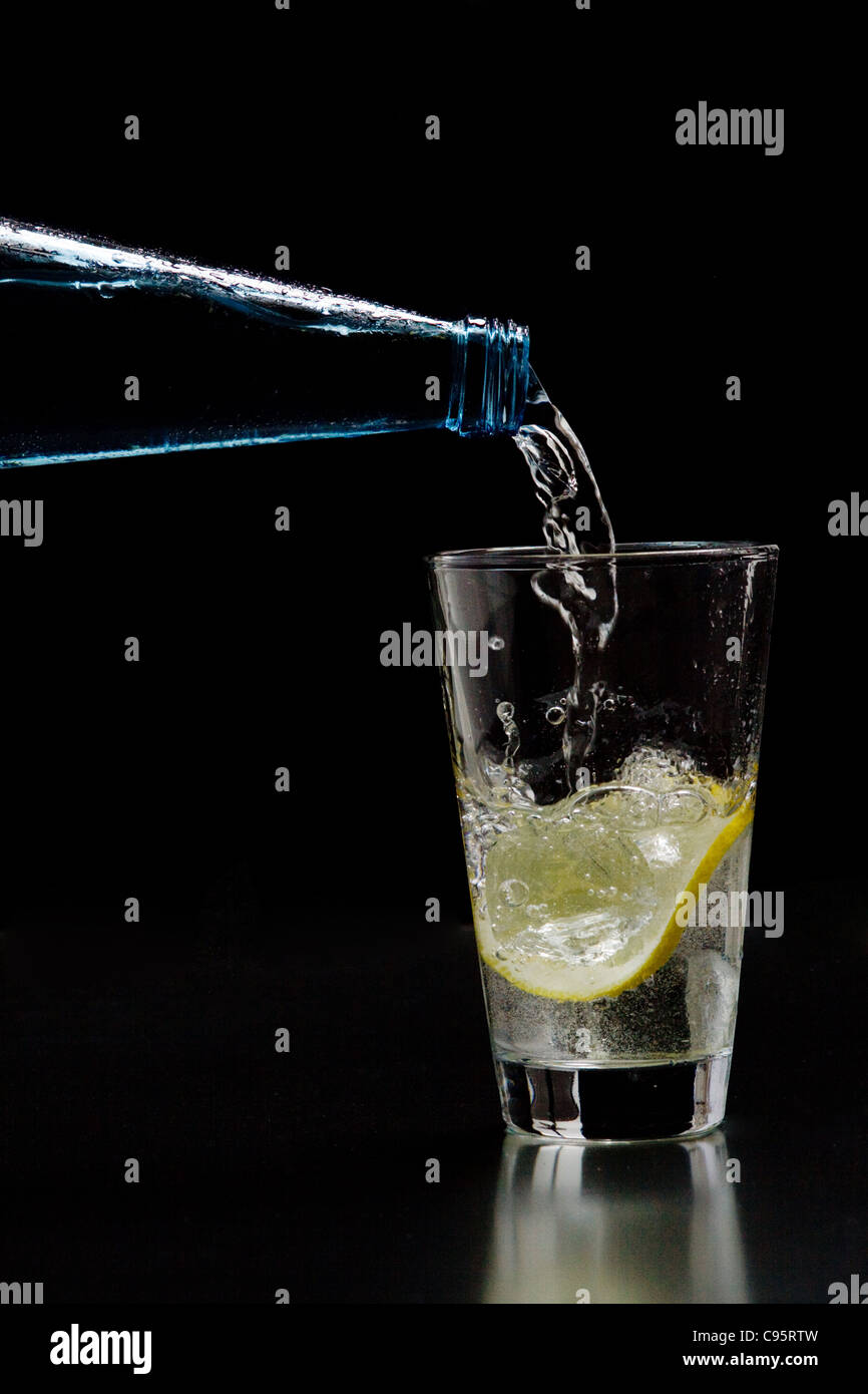 L'acqua minerale è versata in un bicchiere con ghiaccio e limone Foto Stock