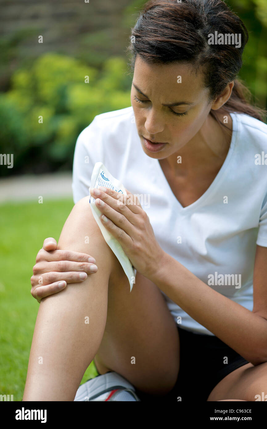 Donna applicando una confezione di ghiaccio al suo ginocchio infortunato. Foto Stock