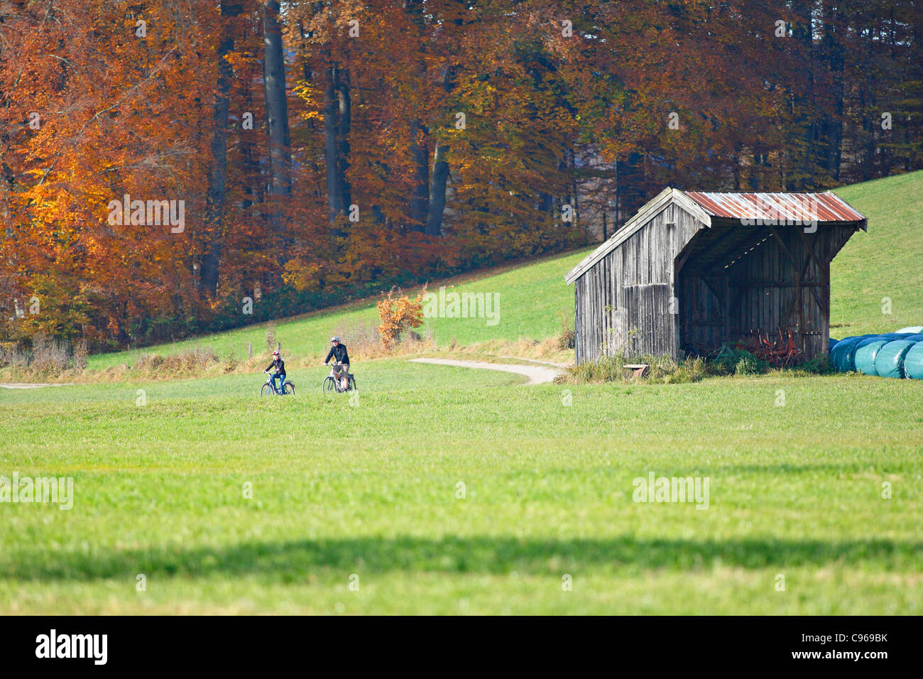 Ciclisti passando un Farmshed bavarese, Chiemgau Alta Baviera Germania Foto Stock