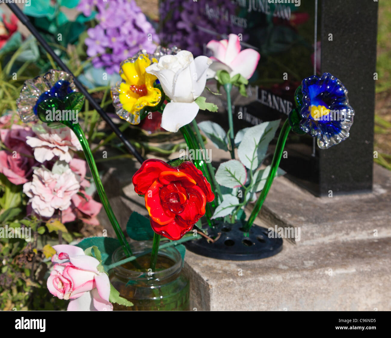Dettaglio del vetro colorato e fiori di seta accanto a una lapide su una tomba. Il cimitero. Foto Stock