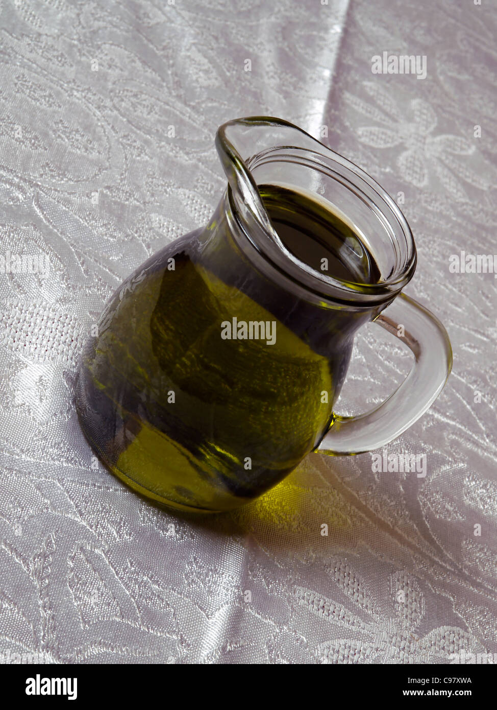 Caraffa di vetro contengono olio di oliva tavola bianco luce del giorno panno bere mangiare cibo mediterraneo Cucina cucinare la cottura di gusto uva oleoso Foto Stock