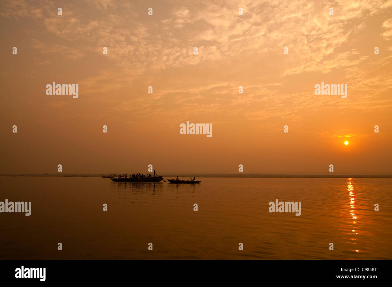 Un sunrise guardando oltre il più sacro dei fiumi in India. Il Gange. Sagome di barche di colline punteggiano l'orizzonte. Foto Stock