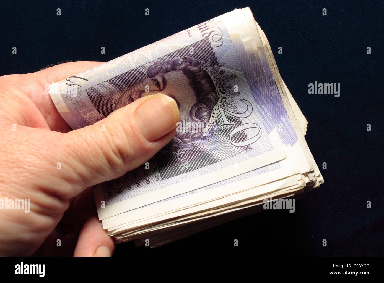 Un batuffolo di £20 note piegato tenuto in mano tra il pollice e le dita Foto Stock