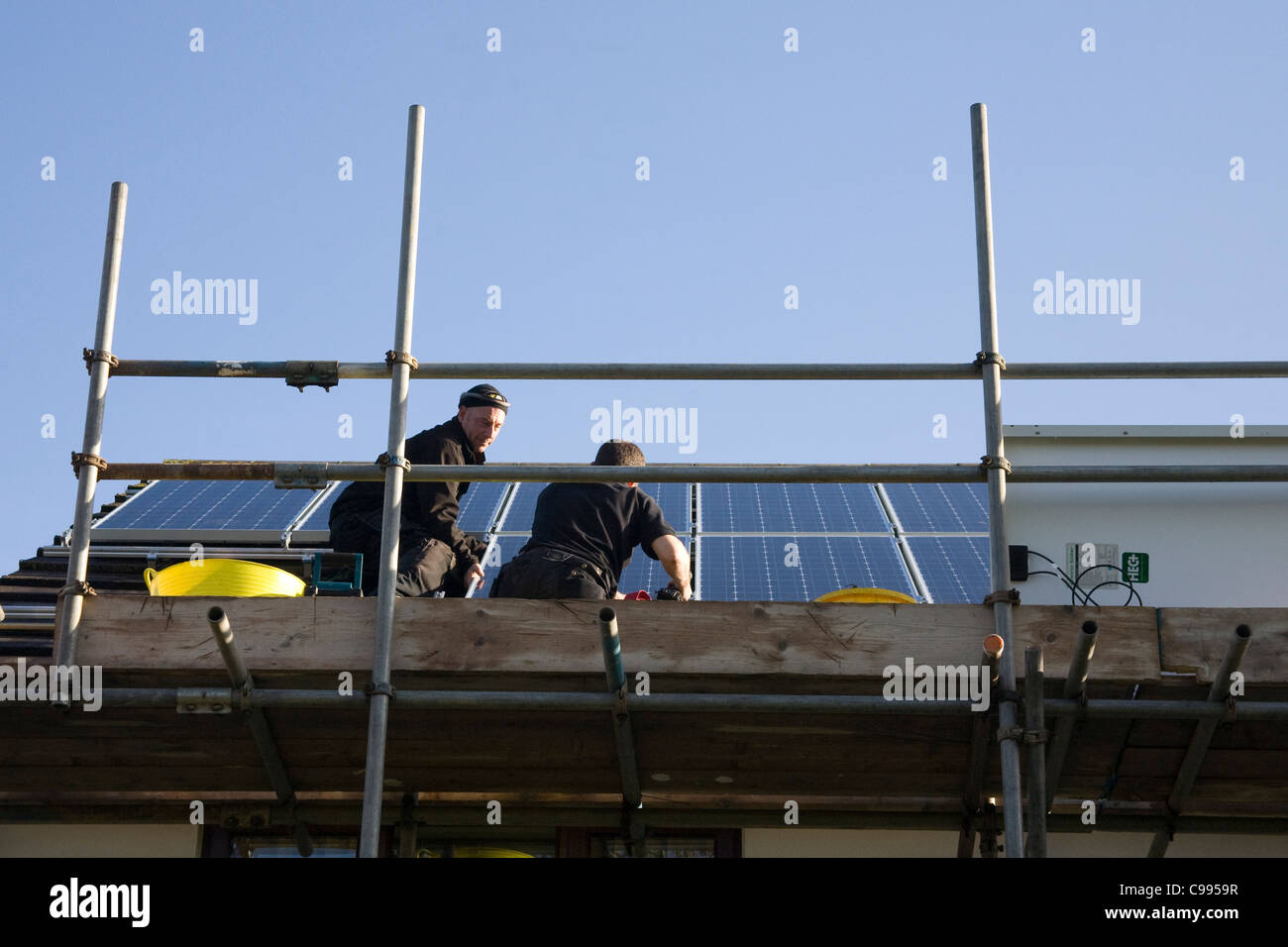 Regno Unito due uomini stavano in piedi su un ponteggio montaggio di pannelli solari su una casa interno tetto sotto il mangime in tariffa regime FIT Foto Stock