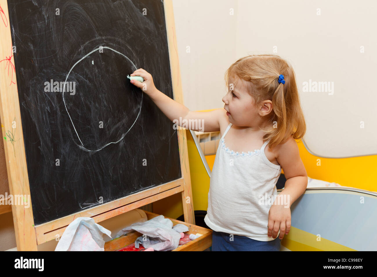 Un piccolo russo ragazza caucasica il disegno con il gesso sulla lavagna in ambiente domestico Foto Stock
