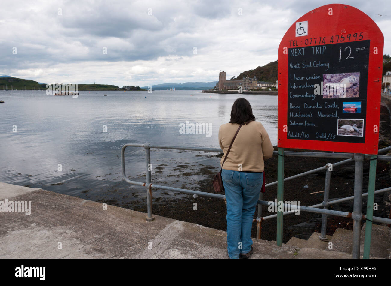 Un turista legge un segno a Oban pubblicità porto di gite in barca e fauna viaggi. Foto Stock