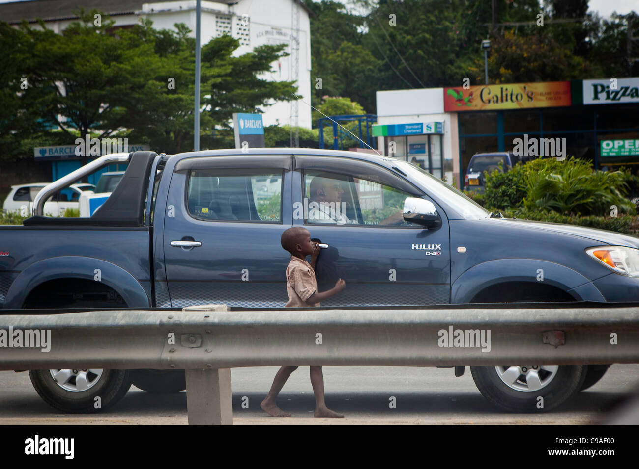 Un bambino di strada a Mombasa, in Kenya per l'accattonaggio denaro da un uomo bianco passato di guida. Foto Stock