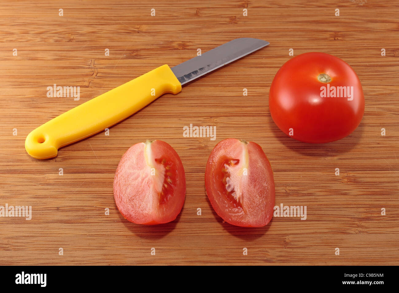 Pomodoro, coltello e due quarti di pomodoro su di un tagliere Foto Stock