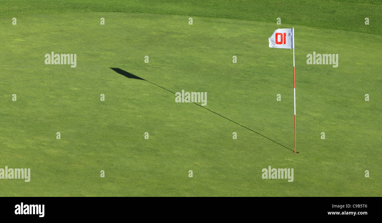 Un pennone e la sua ombra in prossimità del foro su un verde campo da golf. Foto Stock