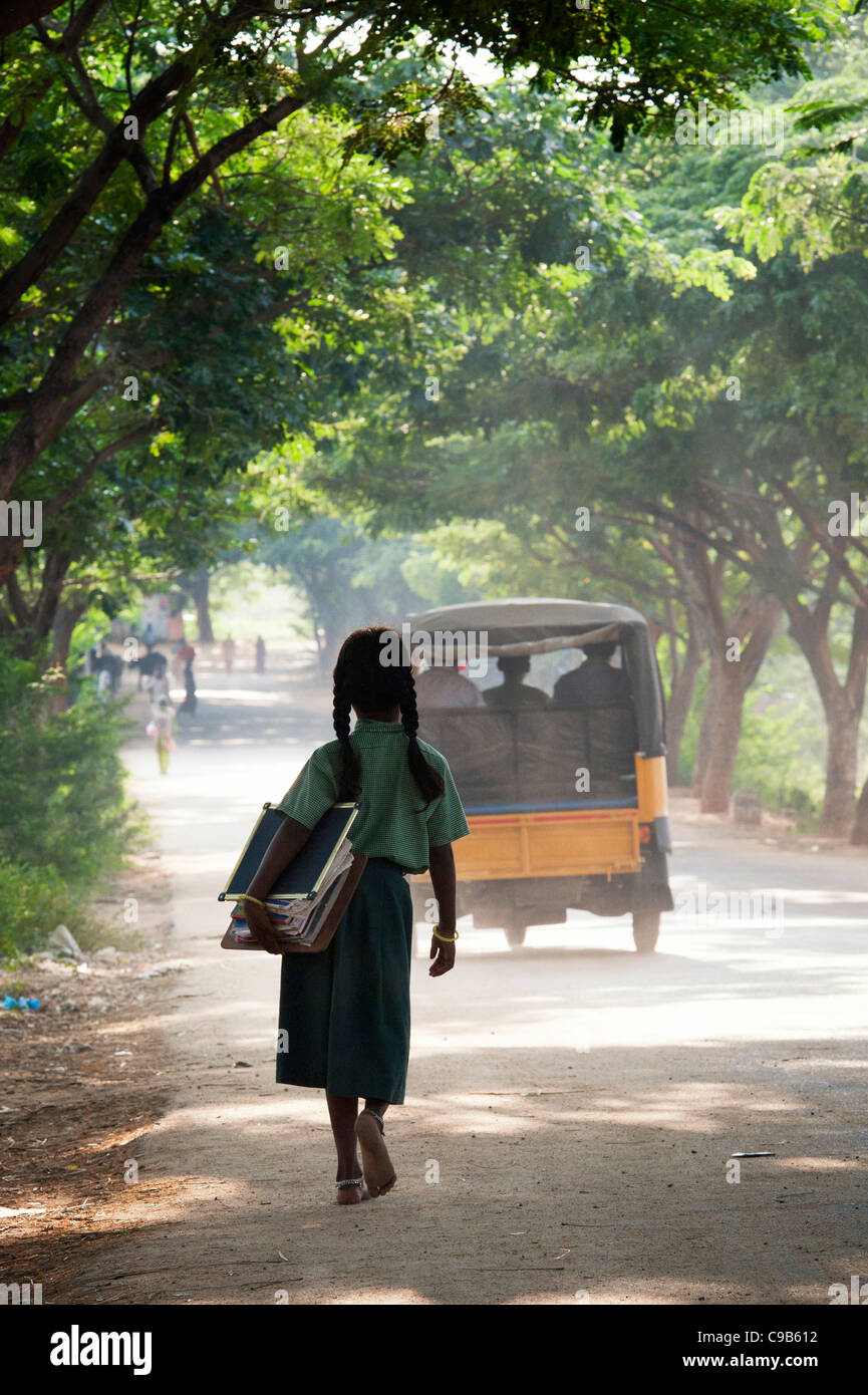 Indian School girl silhouette andare a scuola a piedi il trasporto di libri sotto una strada fiancheggiata da alberi. Andhra Pradesh, India Foto Stock