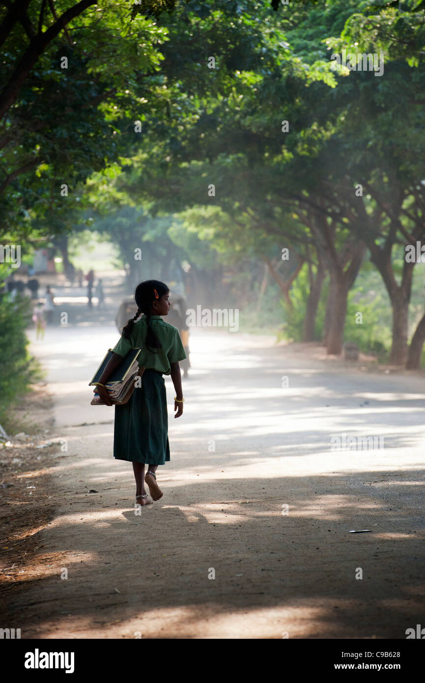 Indian School girl silhouette andare a scuola a piedi il trasporto di libri sotto una strada fiancheggiata da alberi. Andhra Pradesh, India Foto Stock