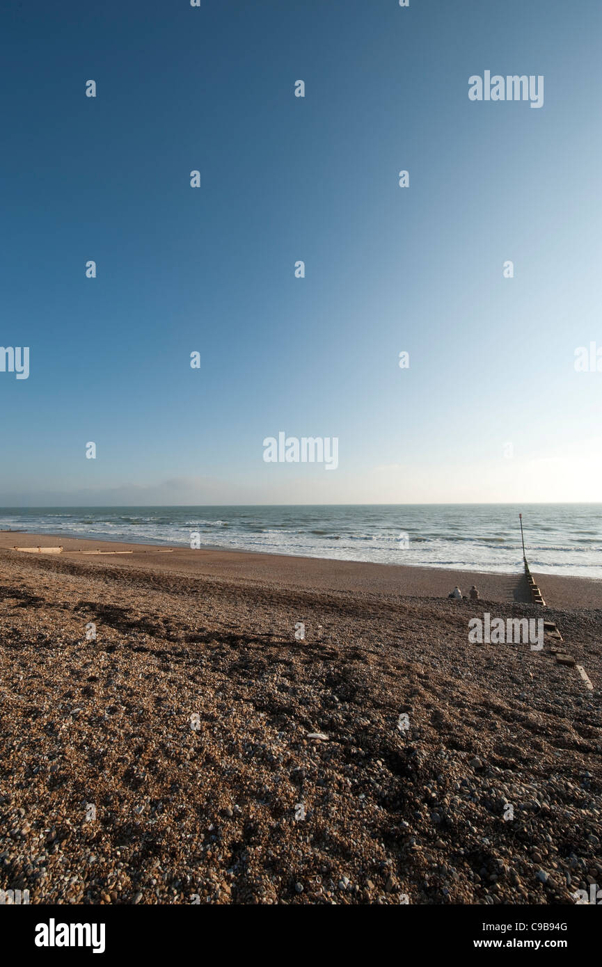 Due persone sedute sulla spiaggia di ciottoli a Bexhill on Sea, East Sussex, Inghilterra in autunno sera la luce solare Foto Stock