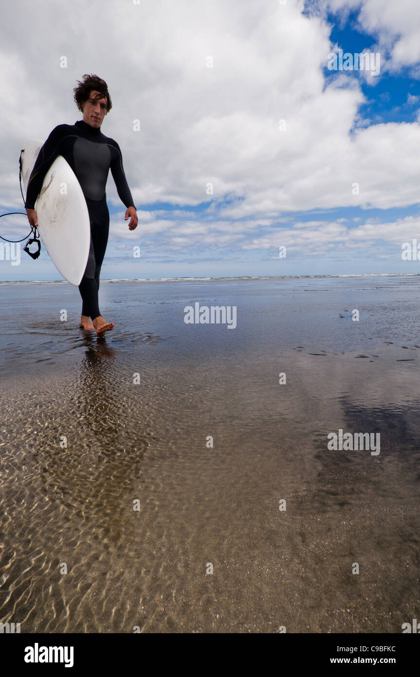 Surfer camminano sulla spiaggia con la tavola da surf, Raglan, New Zealnad Foto Stock