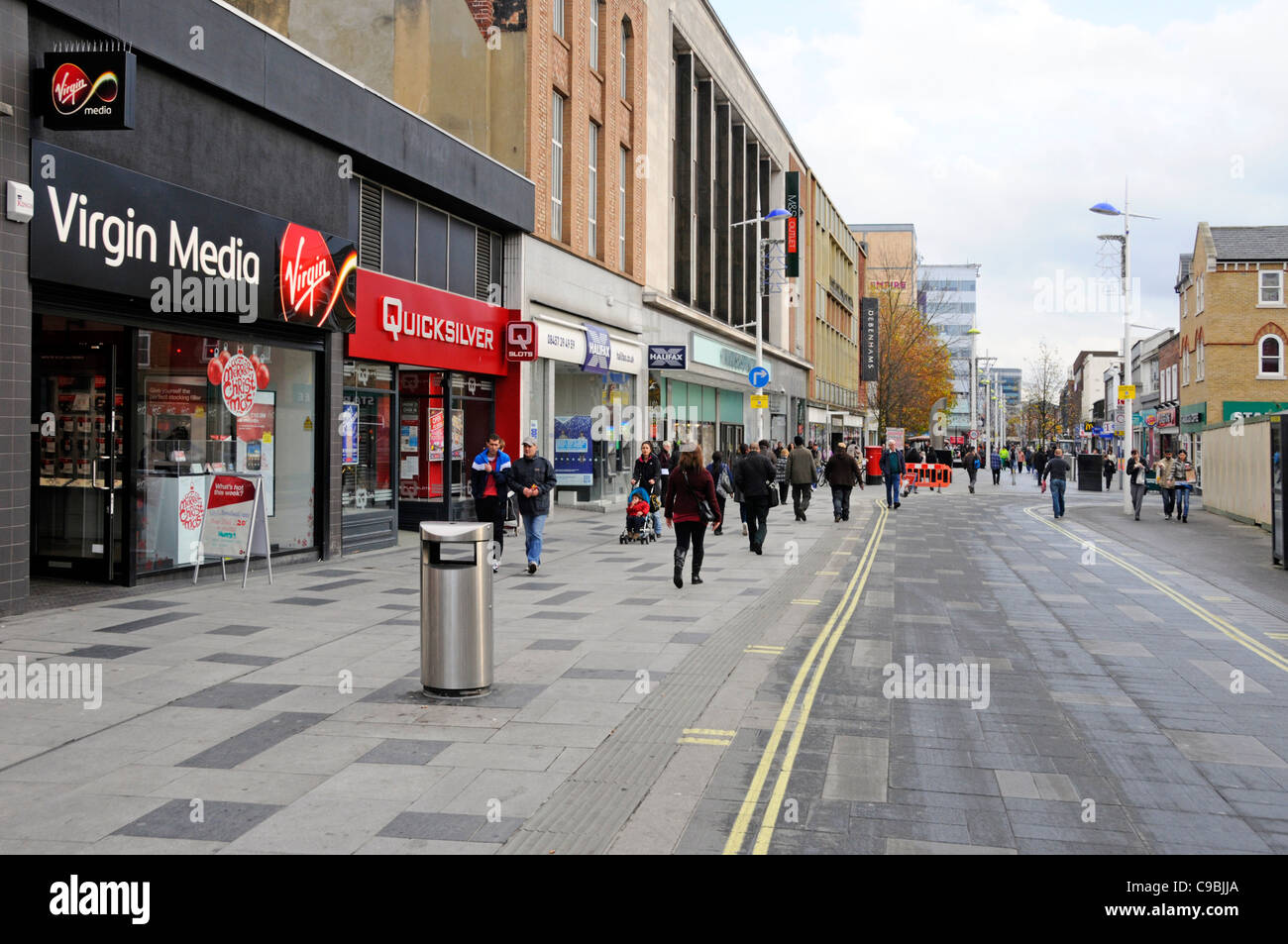 Autunno street scene Virgin Media e altre attività di vendita al dettaglio negozi & negozi lungo il centro città high street con persone shopping a Slough Berkshire REGNO UNITO Foto Stock