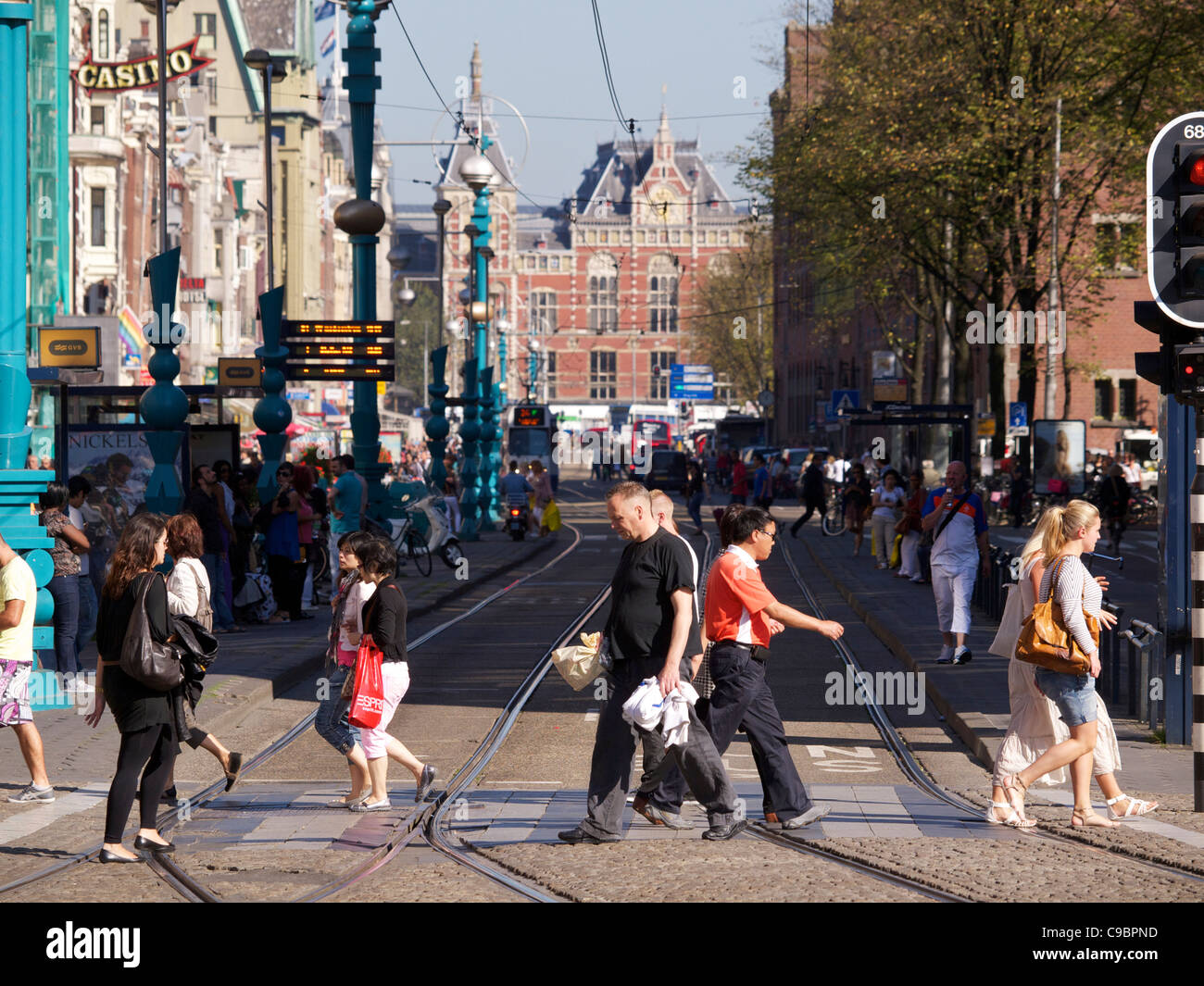 Le persone che attraversano le Strada Damrak con la stazione centrale di Amsterdam in background, Paesi Bassi Foto Stock