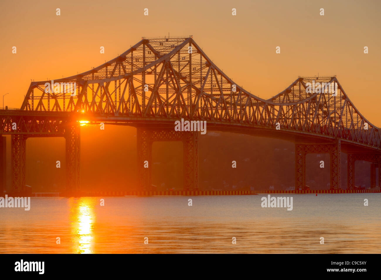 Il sole tramonta dietro il Tappan Zee Bridge e si riflette sulla superficie del fiume Hudson. Foto Stock