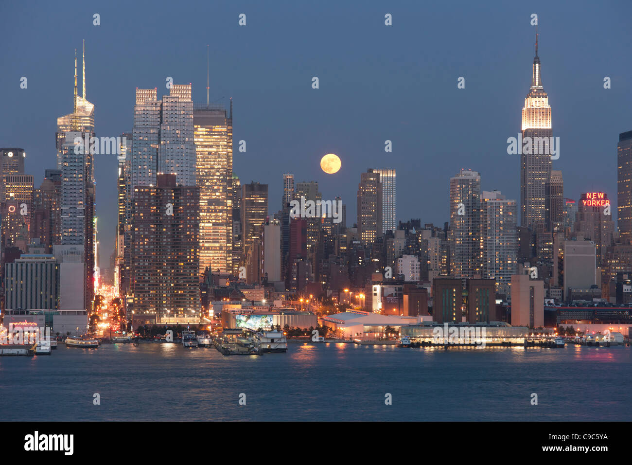 La luna piena sorge sopra la skyline di Manhattan al crepuscolo come visto sopra il fiume Hudson da New Jersey Foto Stock