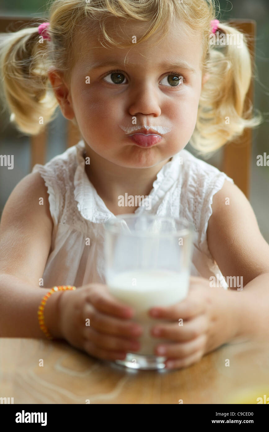 Bambina con latte i baffi gustando un bicchiere di latte Foto Stock