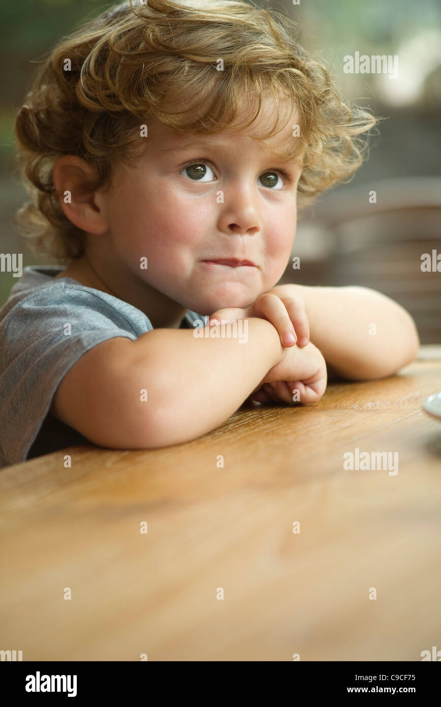 Little Boy mento di appoggio sui bracci, guardando lontano nel pensiero, ritratto Foto Stock