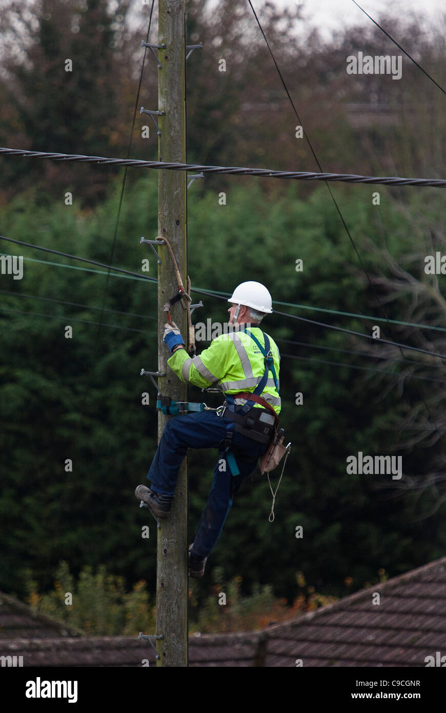 Un BT (British Telecom ) engineer si arrampica su un palo del telegrafo per eseguire controlli di manutenzione. Foto Stock