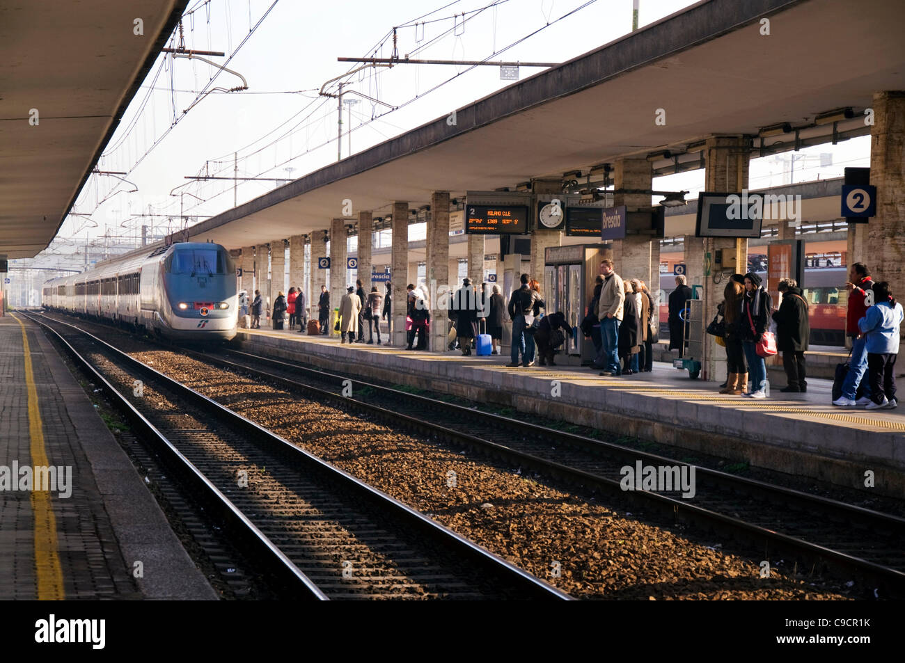 Treno Express arriva presso la stazione ferroviaria di Brescia da Milano passenegers attendere sulla piattaforma Foto Stock