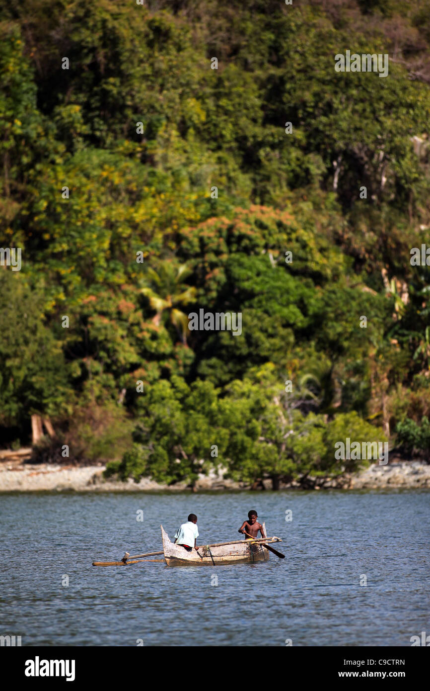 Due giovani ragazzi 8-11 anni paddle loro outrigger piroga off Mamoko isola, Madagascar. La foresta tropicale in background. Foto Stock