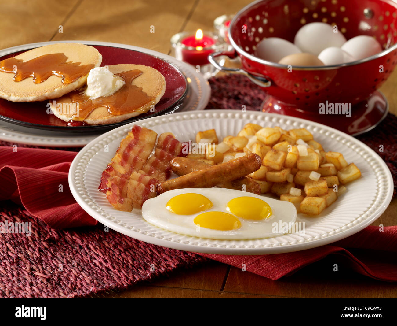 Uova, salsicce, bacon e patate prima colazione con una pila di frittelle Foto Stock