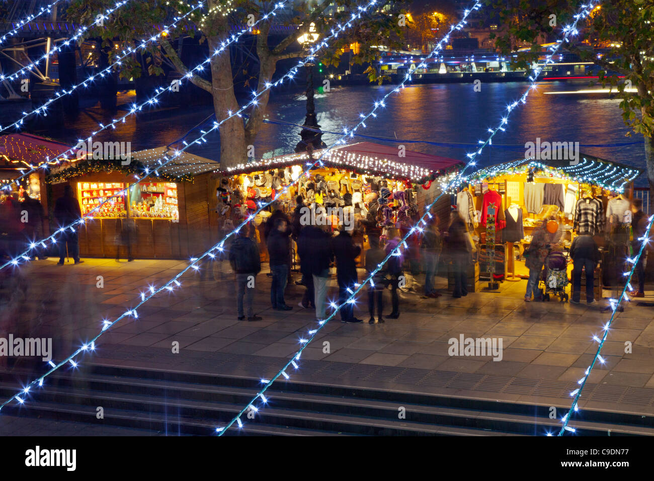Natale Tedesco le bancarelle del mercato sulla South Bank di Londra di Notte, guardando attraverso le linee di luci di Natale Foto Stock