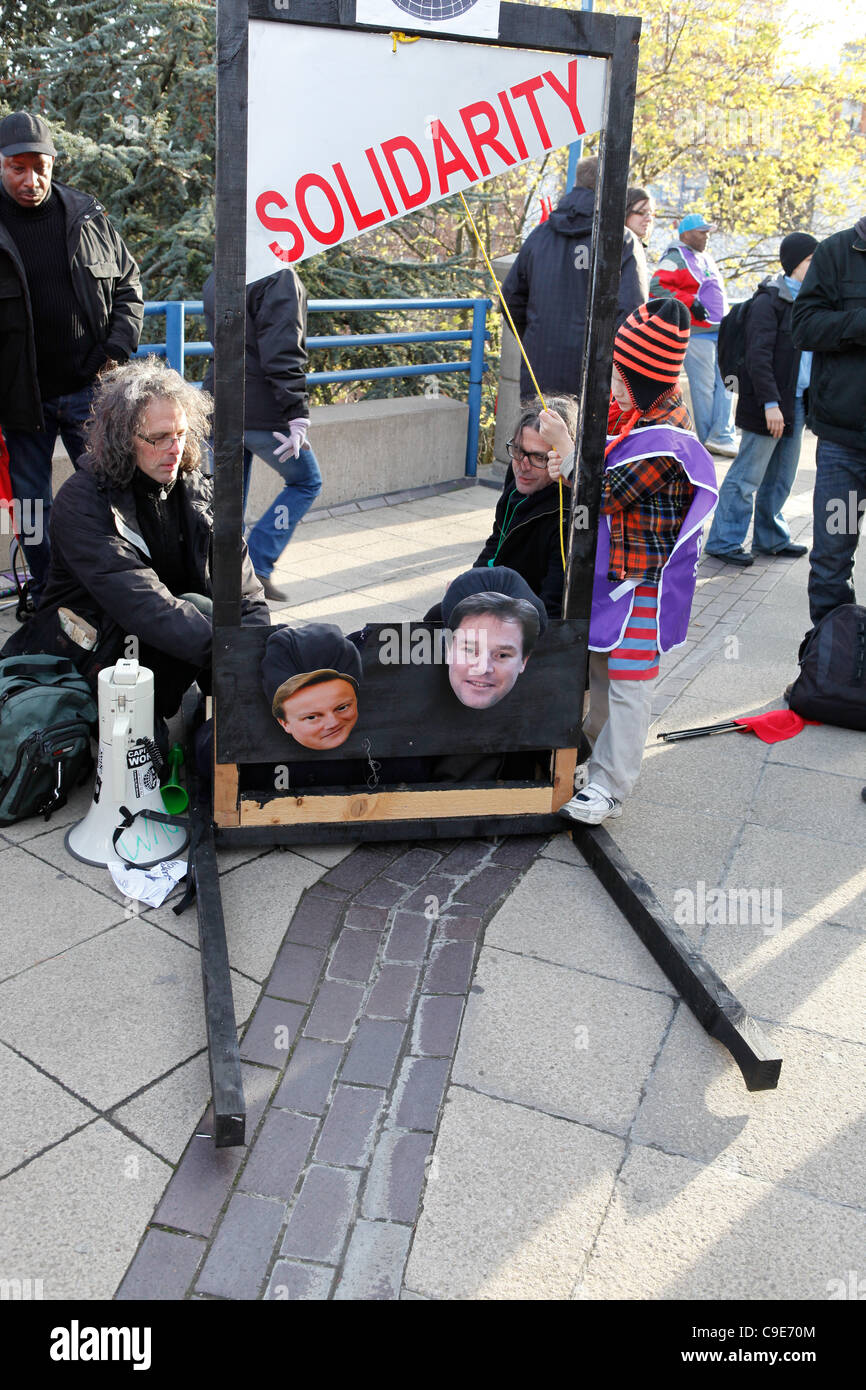 Birmingham, Regno Unito. 30 Novembre, 2011. Una ragazza opera una finta ghigliottina a 'decapitato' Primo Ministro David Cameron e il Vice Primo Ministro Nick Clegg durante le proteste colpendo i lavoratori pubblici in Birmingham. Foto Stock
