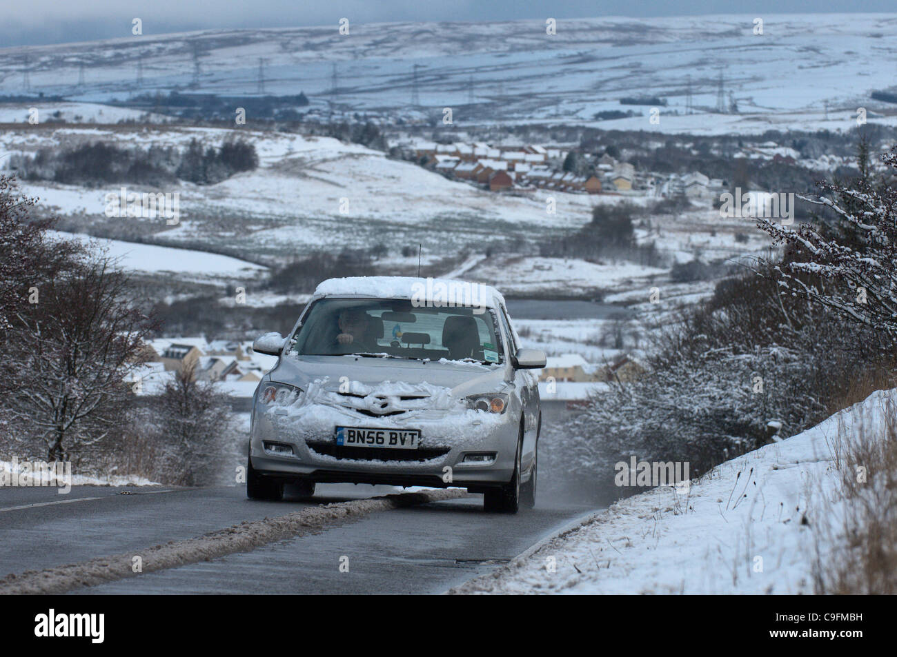 Una vettura impiega una strada fuori Brynmawr, la città più alta in Galles - La prima neve arriva sul Parco Nazionale di Brecon Beacons, Wales, Regno Unito. Foto Stock