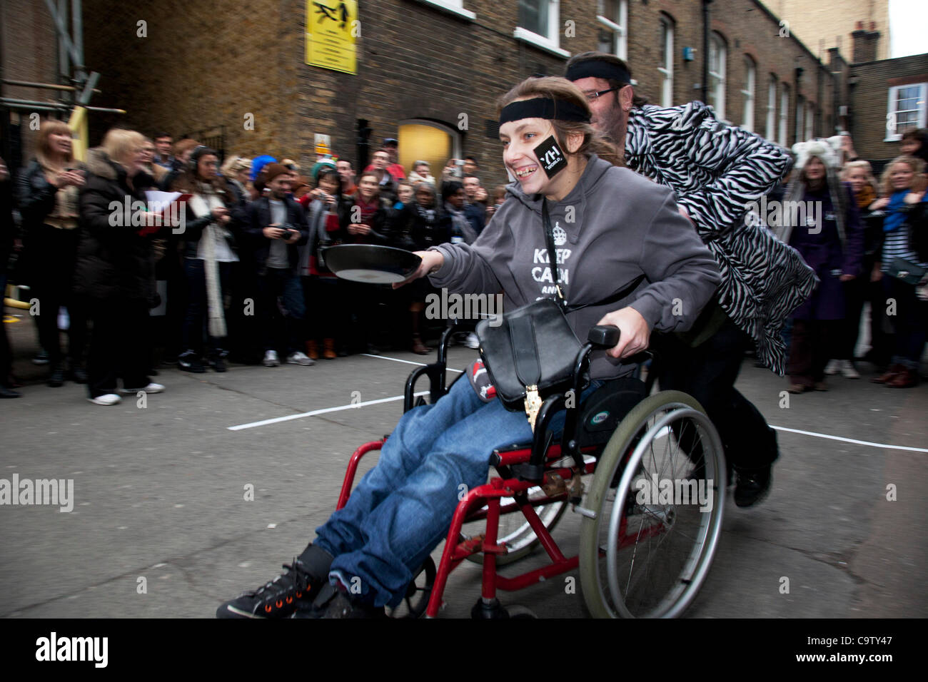 Londra. 21 feb 2012. Un concorrente disabili presso la grande Spitalfields Pancake Race il Martedì Grasso, pancake giorno e alla Old Truman Brewery, Londra, Regno Unito. Squadre di quattro persone dress up in costume di competere. Organizzato da arti alternative la raccolta di fondi per beneficenza. Foto Stock