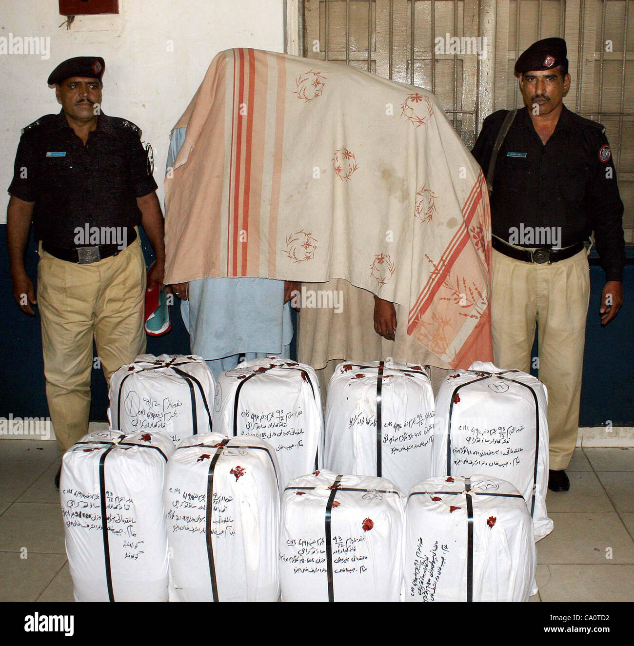 Poliziotti mostrano arrestati accusati (viso coperto con un panno) e recuperato i sacchetti di farmaco (l'eroina) che erano stati sequestrati dalla loro possesso durante la conferenza stampa al Kharadar stazione di polizia a Karachi il giovedì, 15 marzo 2012. Foto Stock