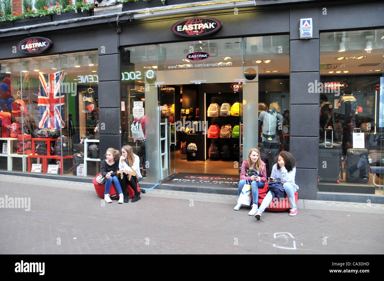 Ragazze sedersi fuori la Eastpak store su Carnaby Street come negozi di  promuovere "Carnaby 20% Shopping parte". Il 31 maggio 2012 Foto stock -  Alamy