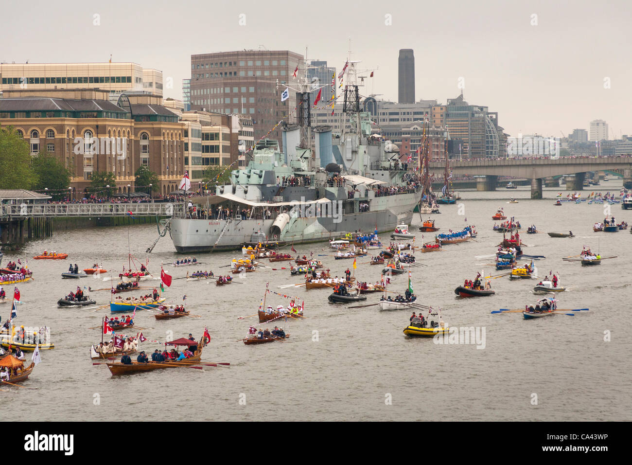 Numerose piccole imbarcazioni procedere lungo il fiume Tamigi passato HMS Belfast come parte del Queen's Thames Diamond Jubilee Pageant, preso dal Tower Bridge, Londra, Regno Unito, 3 giugno 2012. Il Giubileo di Diamante celebra la regina Elisabetta la seconda DEL 60 anni come Capo del Commonwealth. Foto Stock