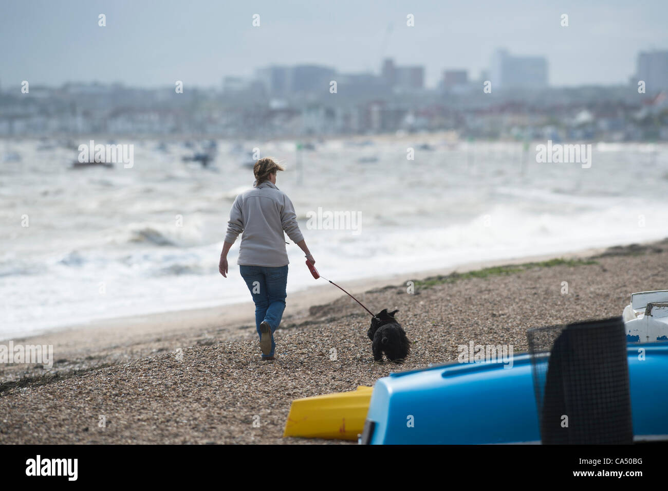 Donna cane a camminare sulla spiaggia in molto ventoso con onde che si infrangono sulla ghiaia. Foto Stock