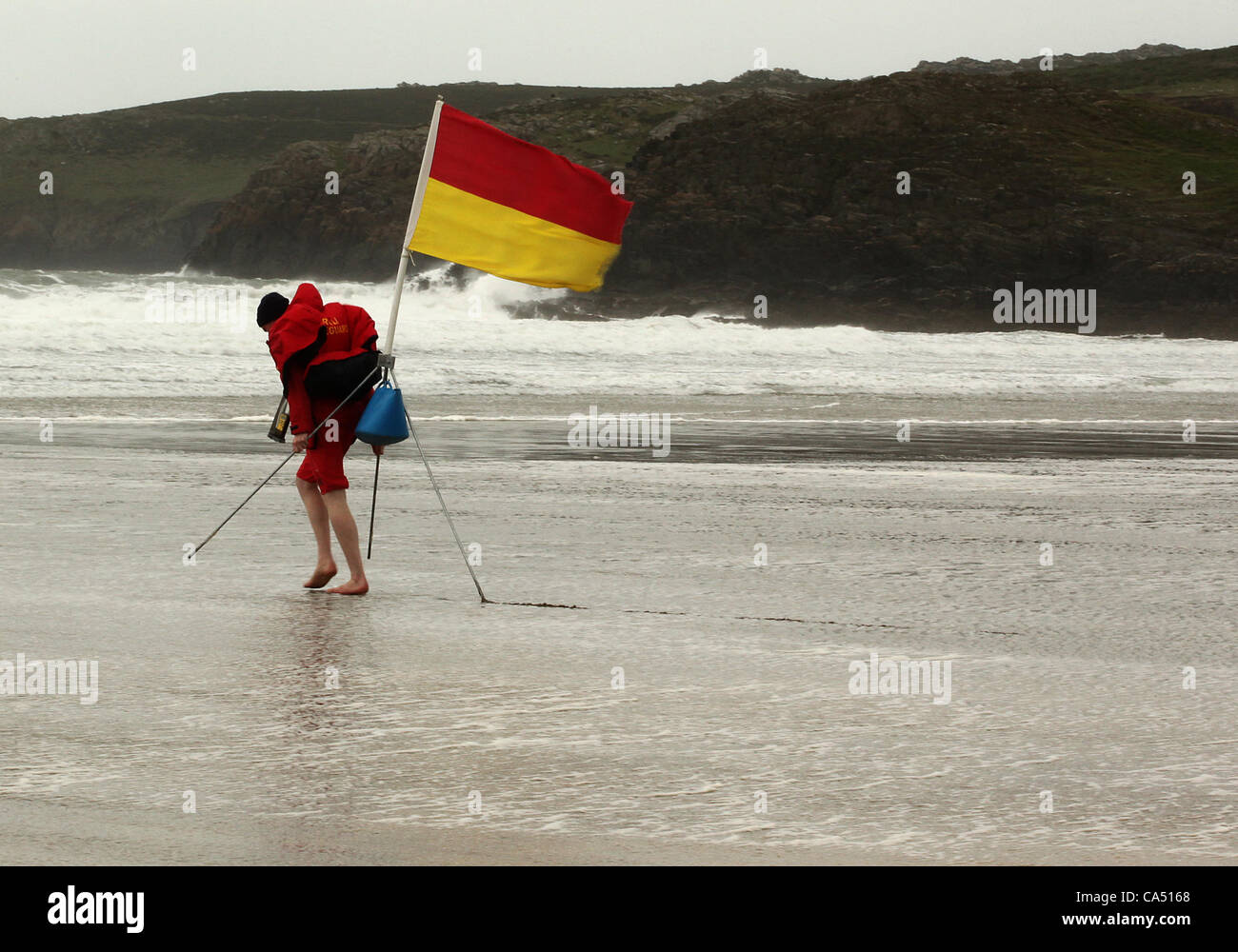 08/06/2012 bagnino locale Oliver Blackstone battaglie contro 60mph winds per spostare un flag di avviso sulla spiaggia di Whitesands Bay South Wales UK Foto Stock