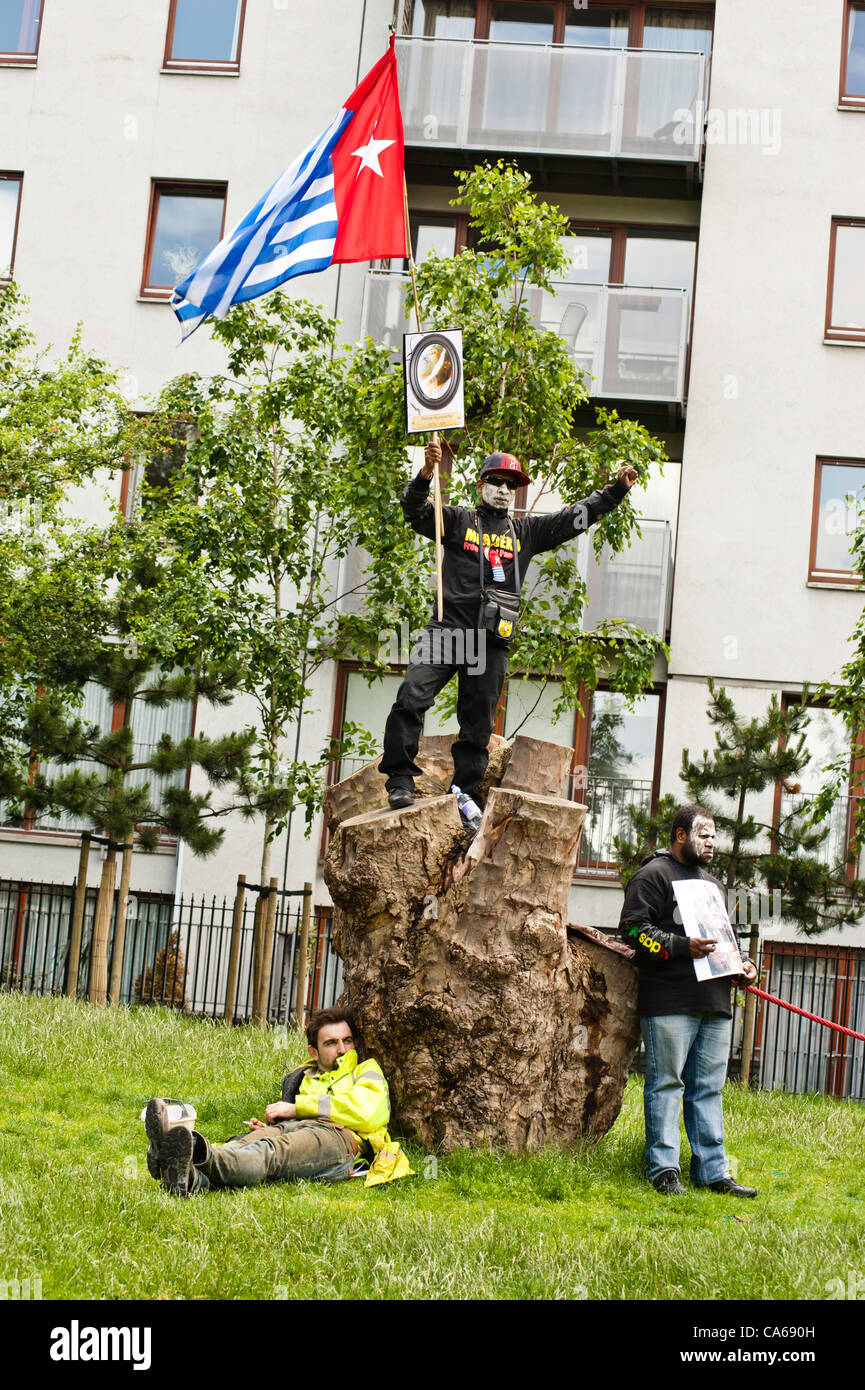 London, Regno Unito - 15 Giugno 2012: un manifestante detiene il Papua Occidentale bandiera mentre un uomo riposa in Altab Ali Park durante il carnevale di sporcizia. Più di 30 gruppi di attivisti da Londra e da tutto il mondo sono venuti insieme per evidenziare il traffico illecito di opere di estrazione mineraria e le aziende di estrazione. Foto Stock