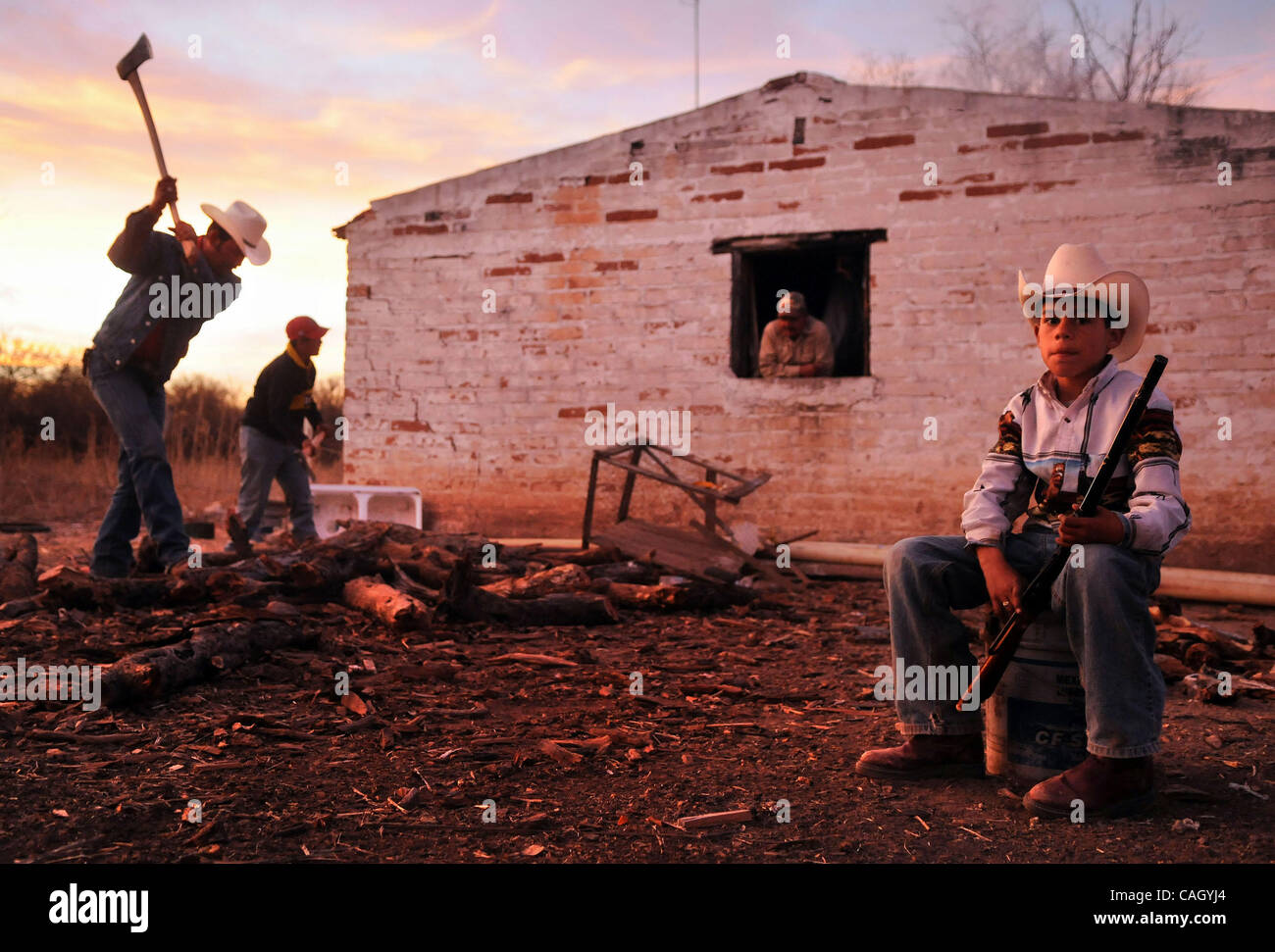 Jan 26, 2008 - Sonora, Messico - AARON CONTRERAS DE MARTIN, 9, siede alto con la sua pistola BB come suo fratello Gesù, 12 E Gesù "fragrante" CONTRERAS, 30, taglia legna da ardere. Roberto Valencia, 62, orologi l'azione dalla finestra del ranch house. Il ranch di bestiame, situato in Sonora Stato del Messico è al Foto Stock