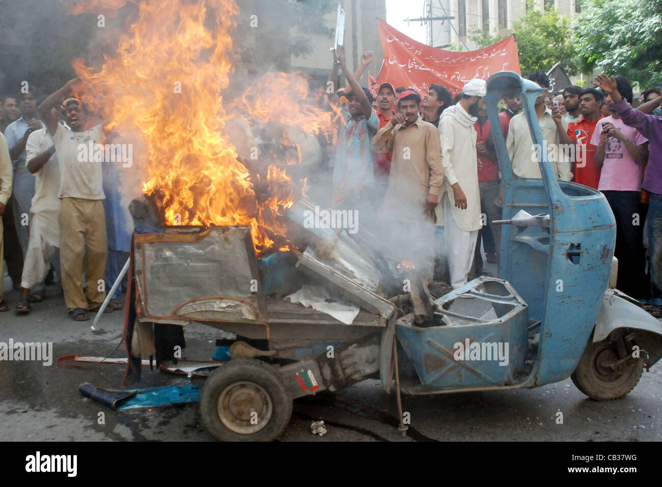 I membri di tutto il Pakistan Associazione GNC raccogliere vicino a bruciare auto-rickshaw chant slogan contro il carico di gas-spargimento durante la manifestazione di protesta a nord di sui gas company con sede a Lahore Lunedì, 28 maggio 2012. Foto Stock