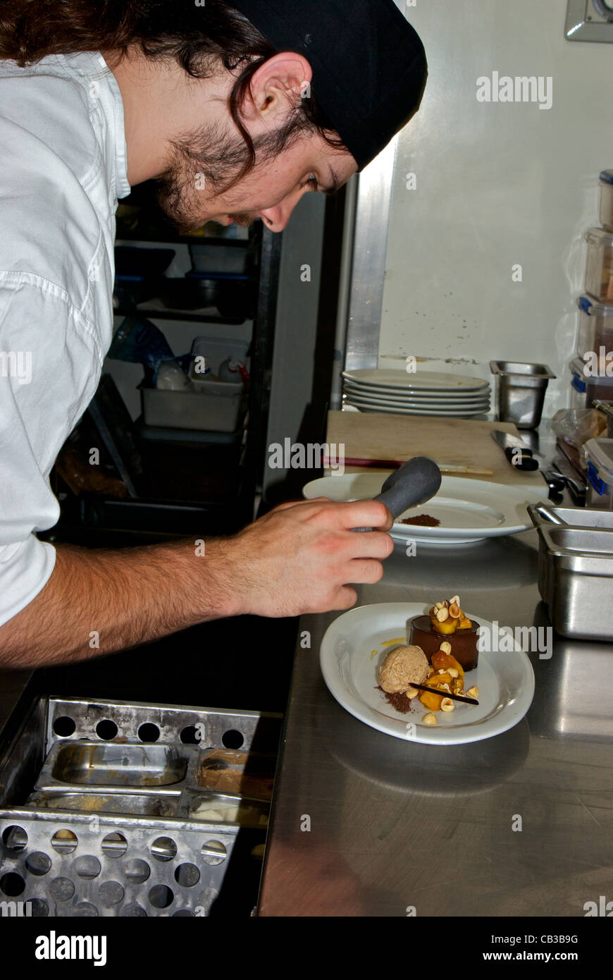 Il giovane chef immissione cucchiaio di gelato a fianco di mousse al cioccolato torta con nocciole e frutta Foto Stock