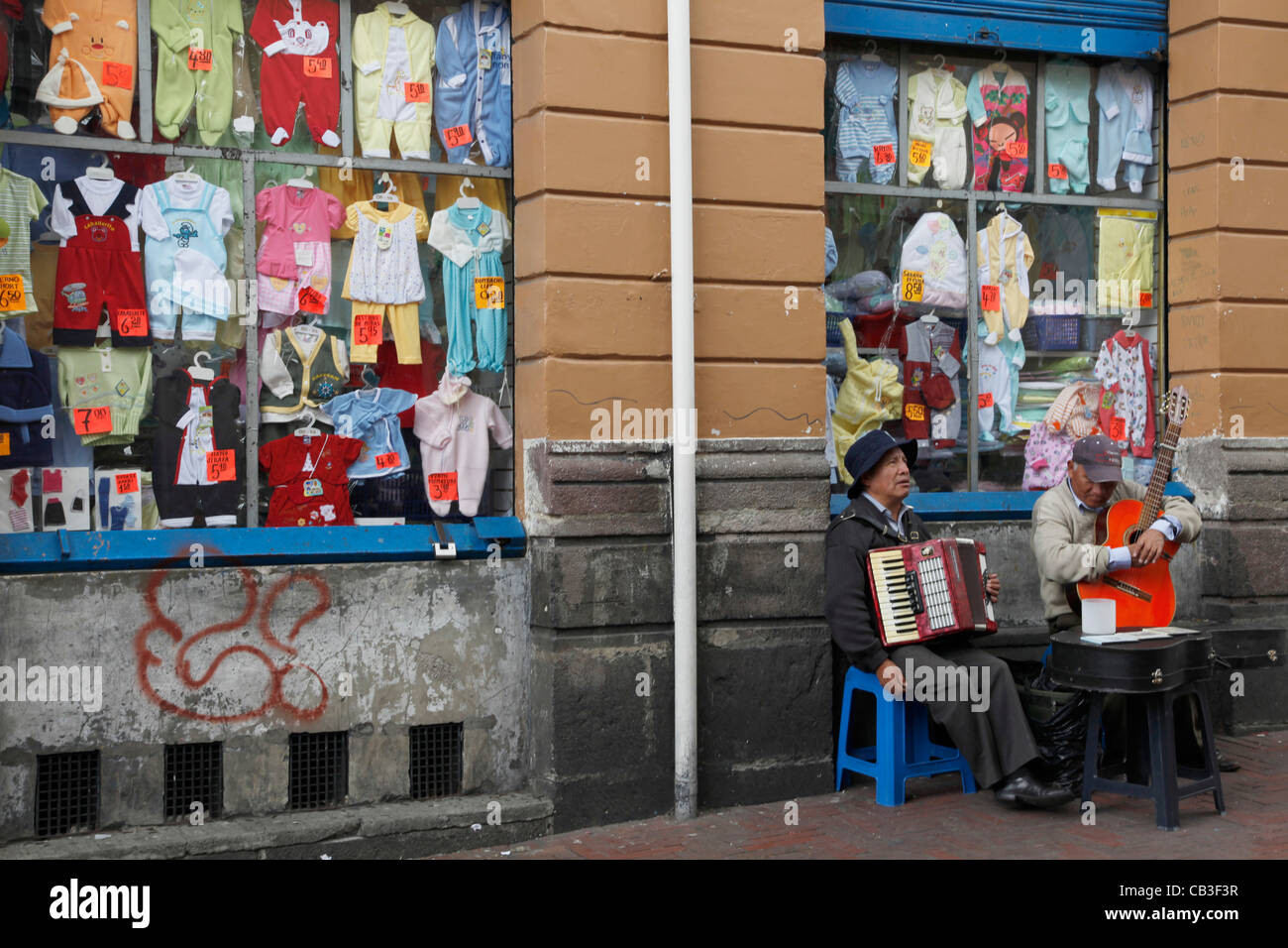 Ecuador. Nativo di uomini Quechua riproduzione di musica per le strade di Quito, con i bambini il negozio di abbigliamento in background Foto Stock