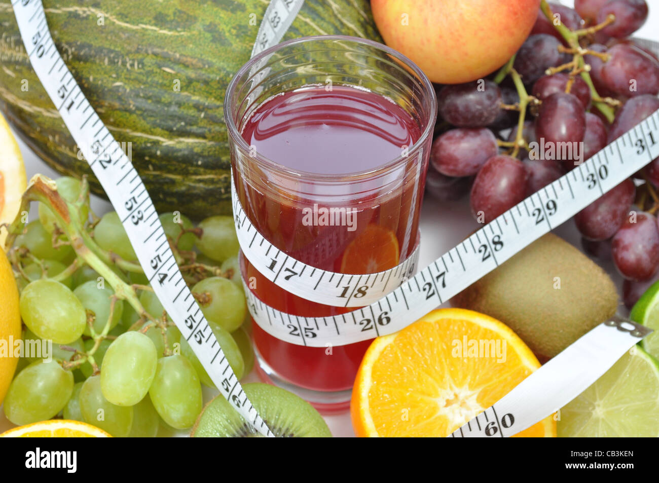 Frutti vari intorno a un bicchiere di succo di frutta e un metro a nastro Foto Stock