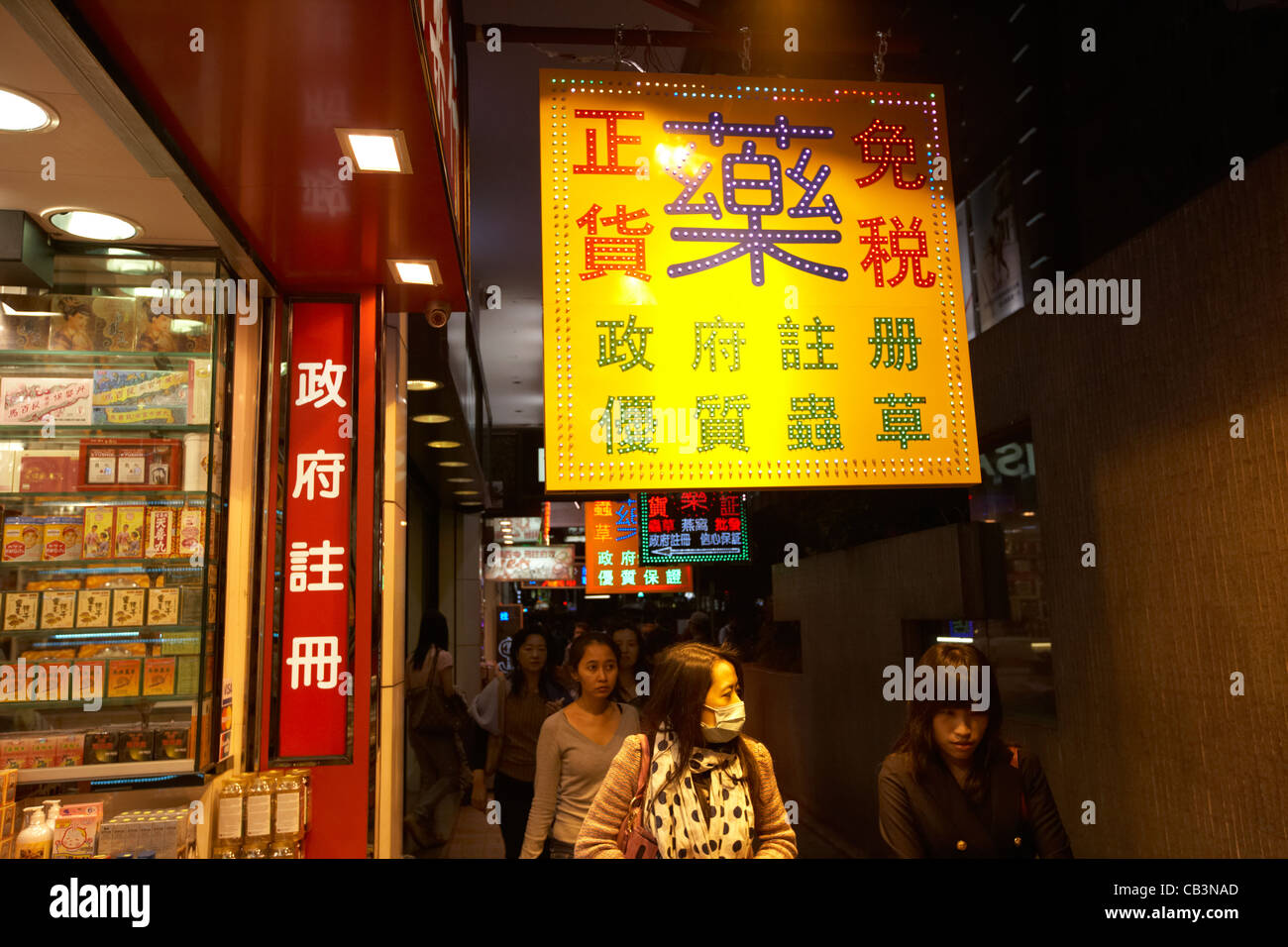 Led segno esterno healthfood shop con la donna che indossa maschera facciale camminando sotto Tsim Sha Tsui di Kowloon hong kong cina della RAS di Hong Kong Foto Stock