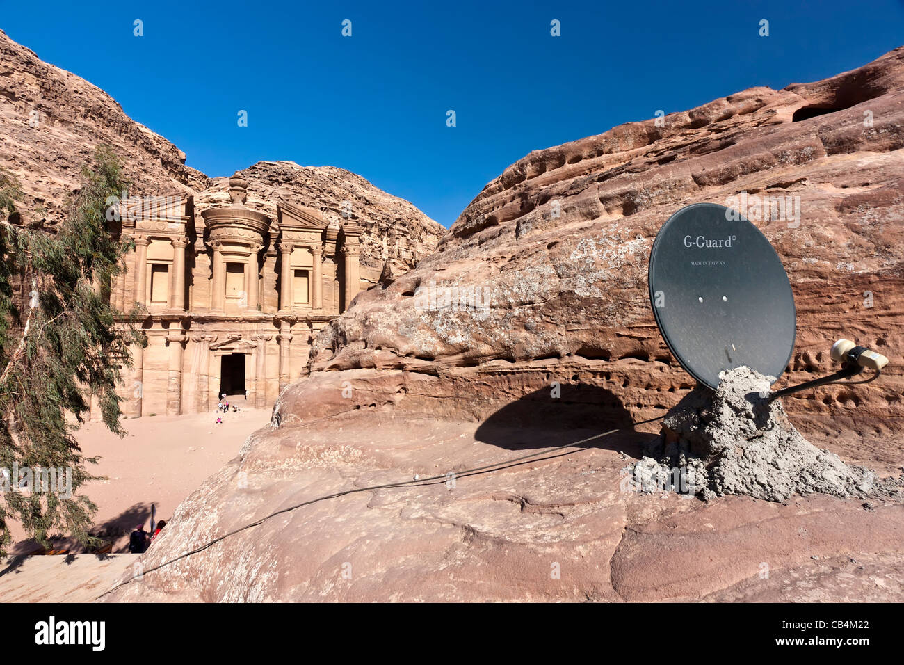 Il vecchio incontra il nuovo - un satellite TV piatto si trova sulla cima di una grotta con la Deir / monastero di Petra in background Foto Stock