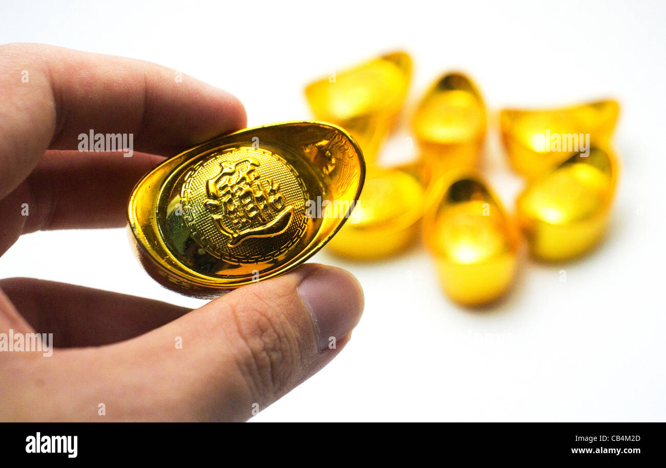Cinese lingotti d'oro, un simbolo di ricchezza per il cinese. Una mano è in possesso di uno dei lingotti d'oro. Foto Stock
