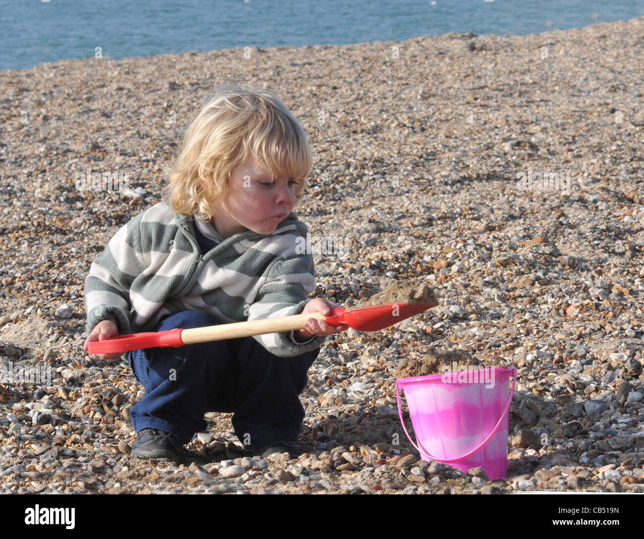 Un Novembre visita alla spiaggia con il suo secchio e capocorda 3 anno vecchio OLIVER GOLDING gode del novembre del sole sulla spiaggia a S Foto Stock